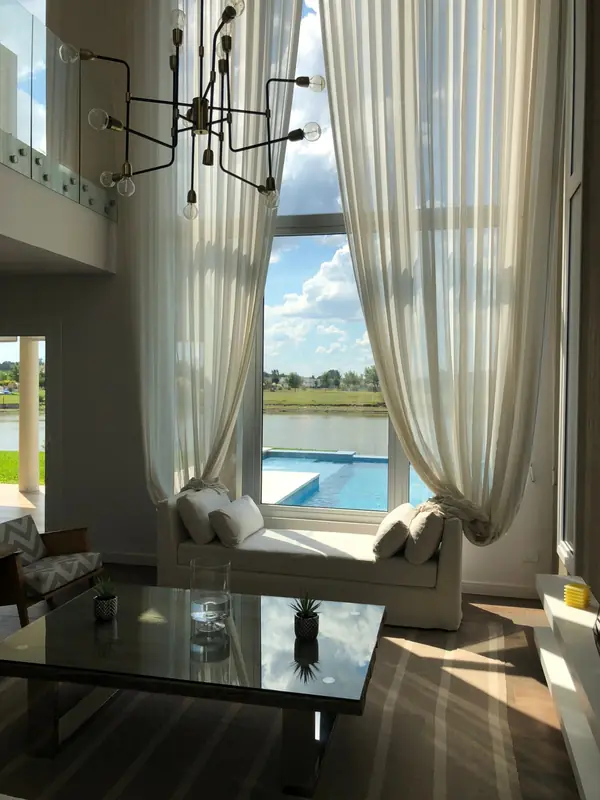 Living de doble altura con ventanal y cortinas hacia la pileta y la laguna